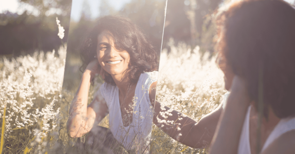 woman looking in a mirror in a field smiling and saying her daily affirmation