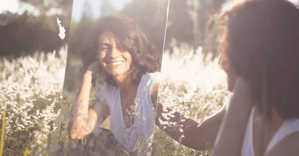 woman looking in a mirror in a field smiling and saying her daily affirmation
