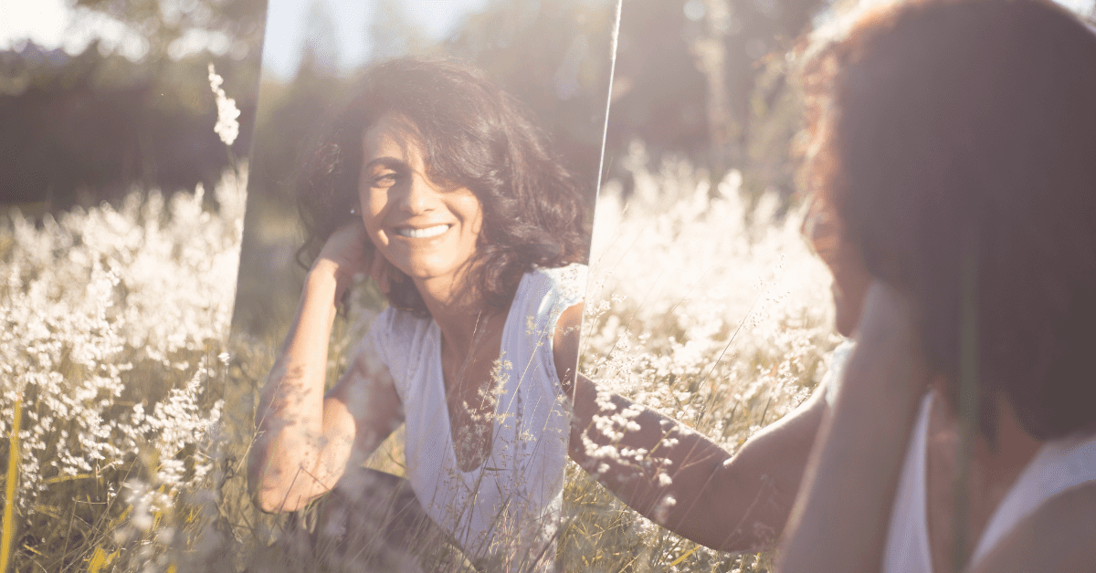 woman looking in a mirror in a field smiling and saying her daily affirmation