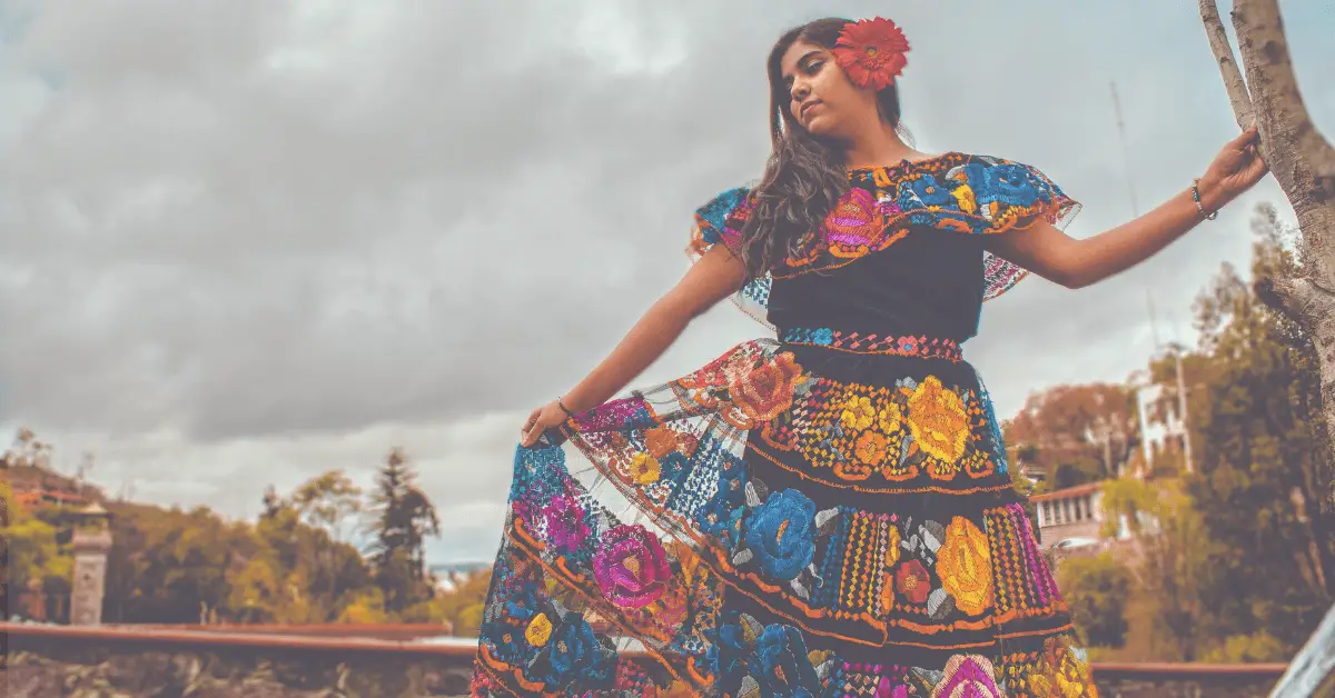 woman in a colorful traditional mexican dress standing next to a tree