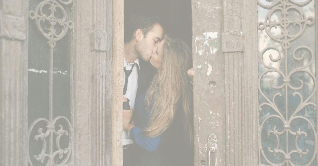 A couple shares a kiss in an old doorway with ornate ironwork.