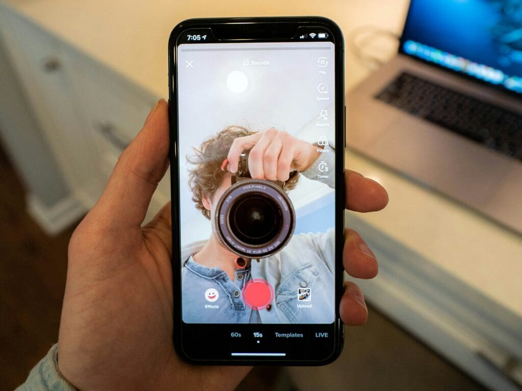 A hand holding a phone with an image of a person taking a picture with a camera.