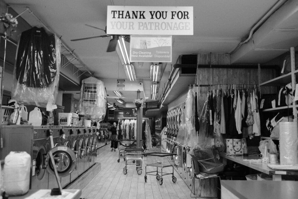black and white photo of the interior of a laundrymat with a sign that says "thank you for your business."
