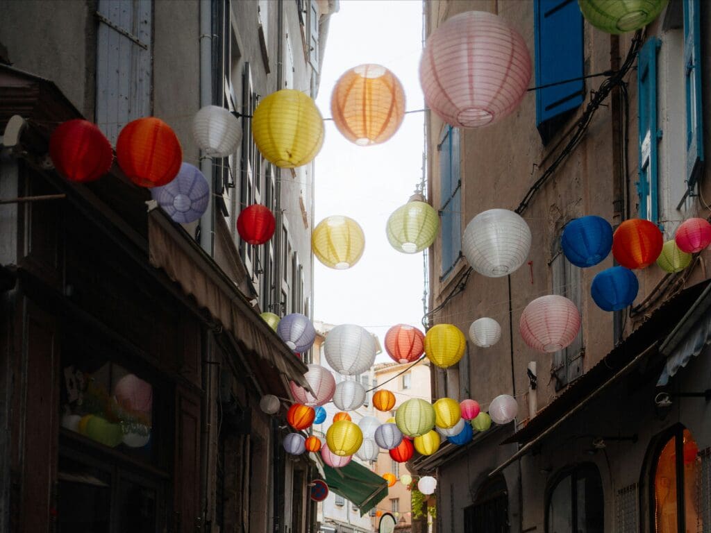A narrow walkway between two buildings with multicolor paper lanterns strung between them.