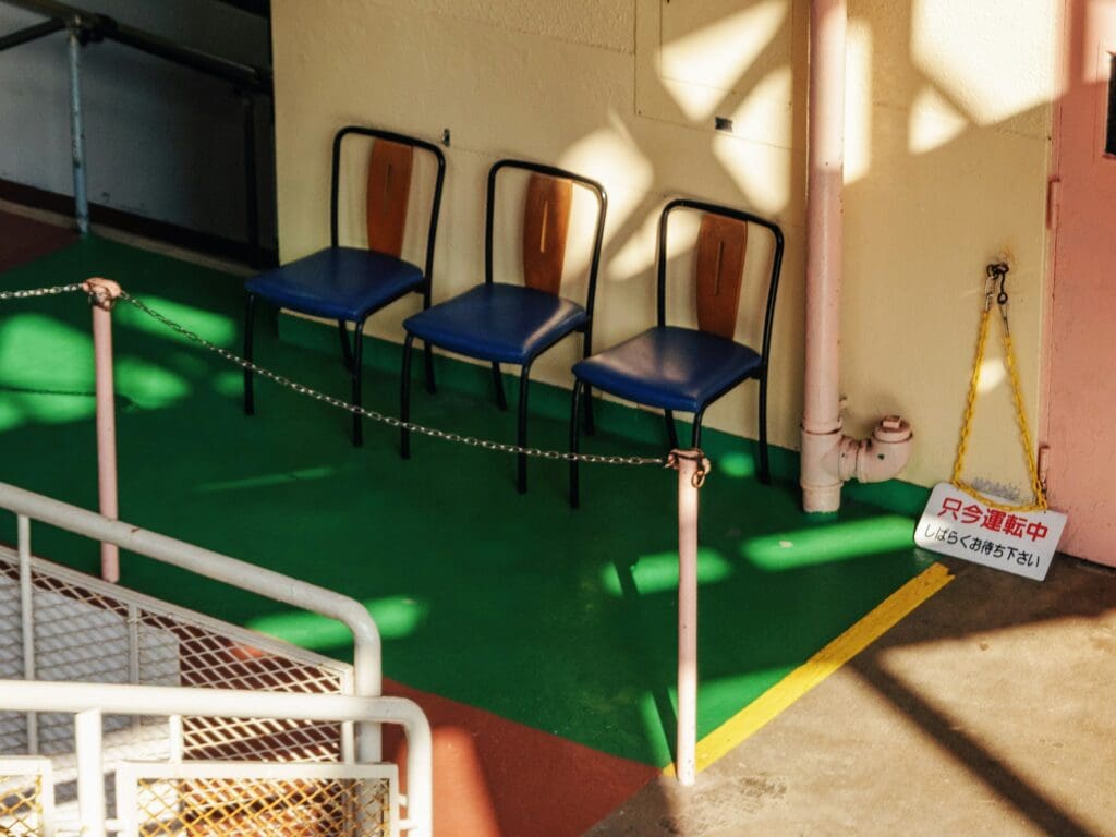 Three blue chairs sitting along a yellow wall in a hall with a dark green floor.