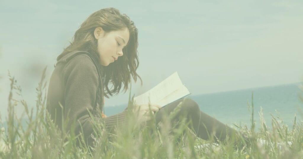 Girl reading a poetry book in the grass by the ocean.