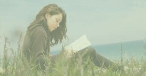 Girl reading a poetry book in the grass by the ocean.