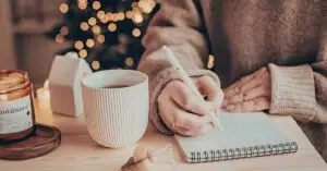woman journaling on notepad with warm drink and candle creating hygee environment