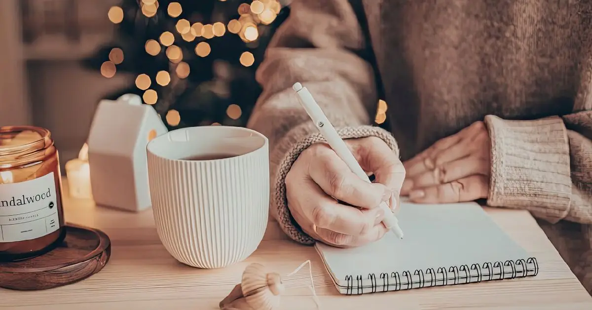 woman journaling on notepad with warm drink and candle creating hygee environment