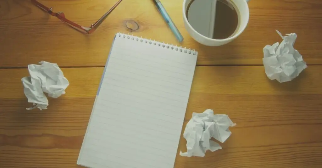 table with empty notepad and wadded up paper expressing writer's block