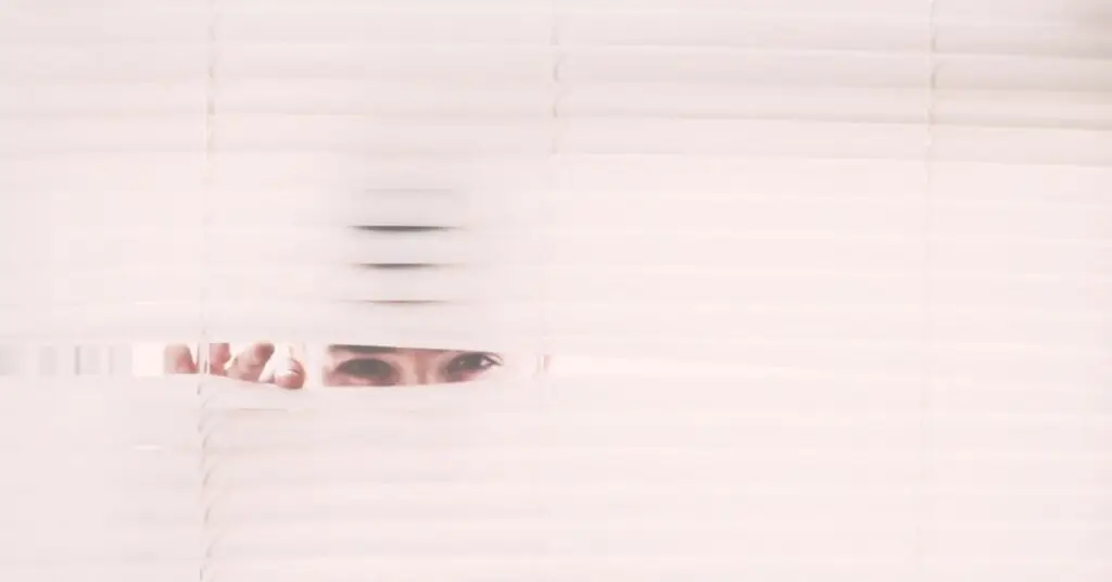 woman peeking through white blinds
