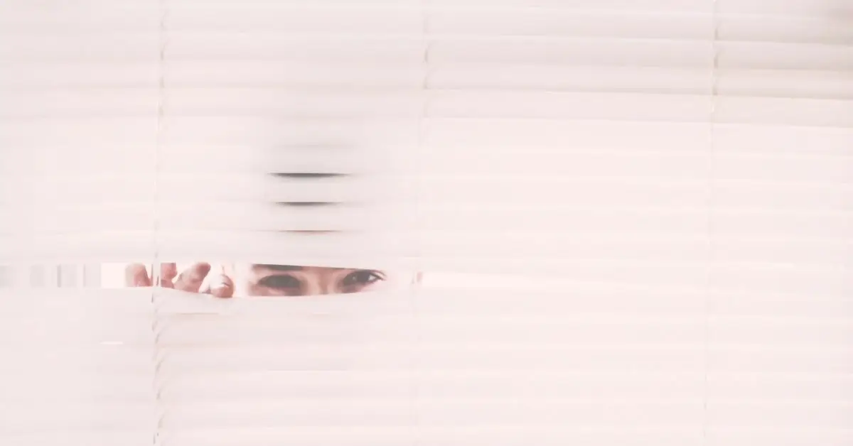 woman peeking through white blinds