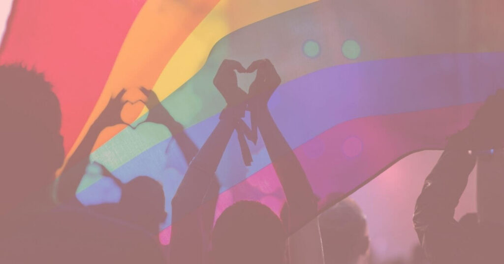 Group making heart symbols with their fingers under a rainbow pride flag