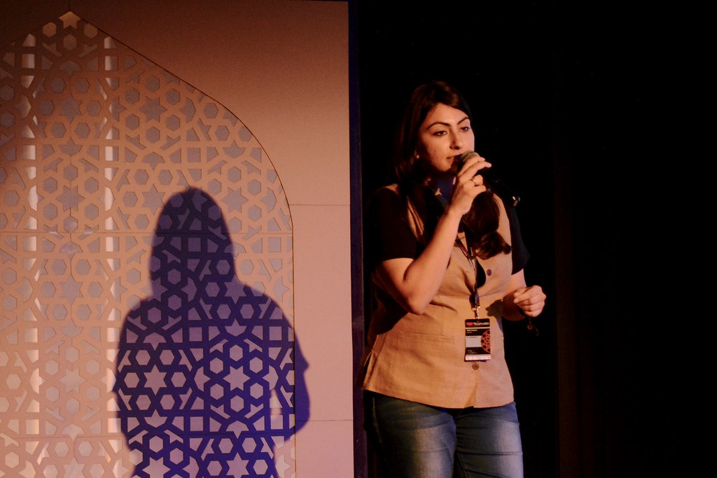 poet aditi angiras speaking on stage with an Indian-style arch behind her.