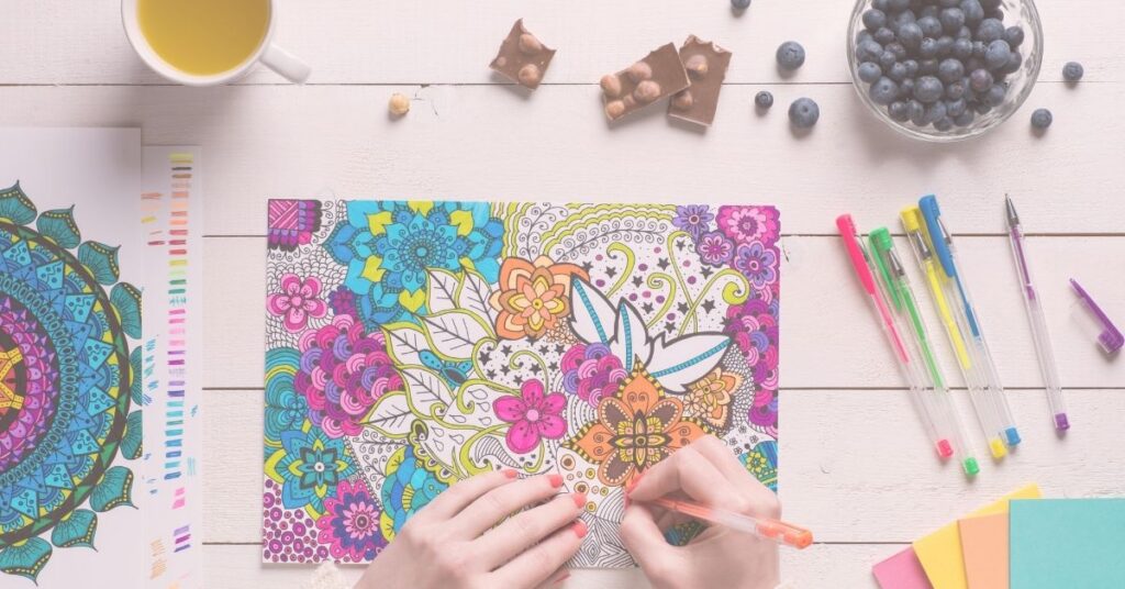 woman at table with snacks and a colorful mandala coloring sheet that's almost completed.