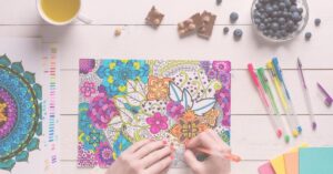 woman at table with snacks and a colorful mandala coloring sheet that's almost completed.