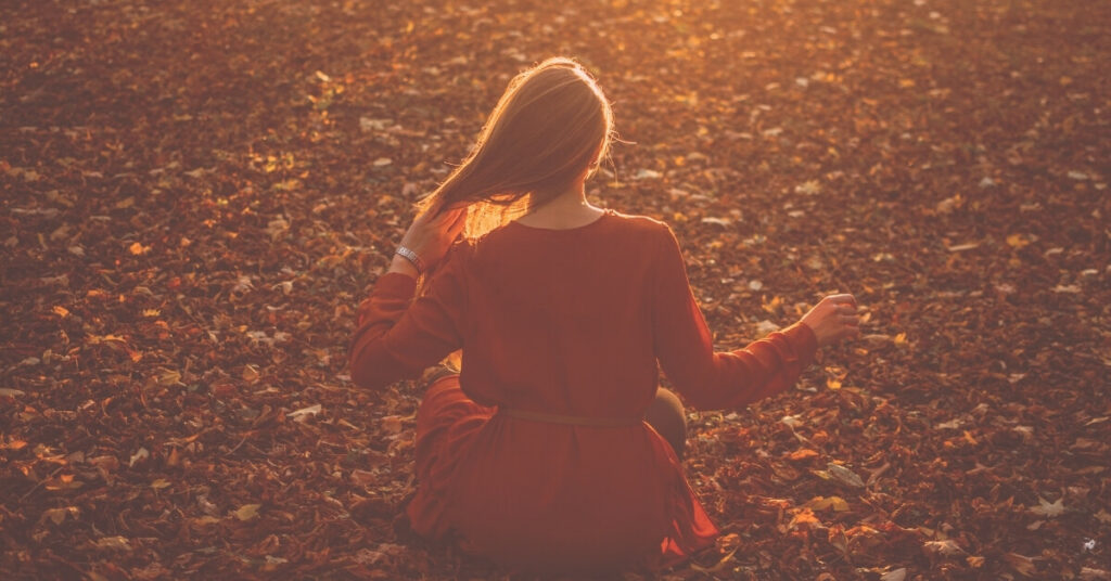 woman in red dress enjoys a quiet meditation among fall leaves