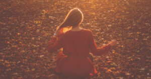 woman in red dress enjoys a quiet meditation among fall leaves