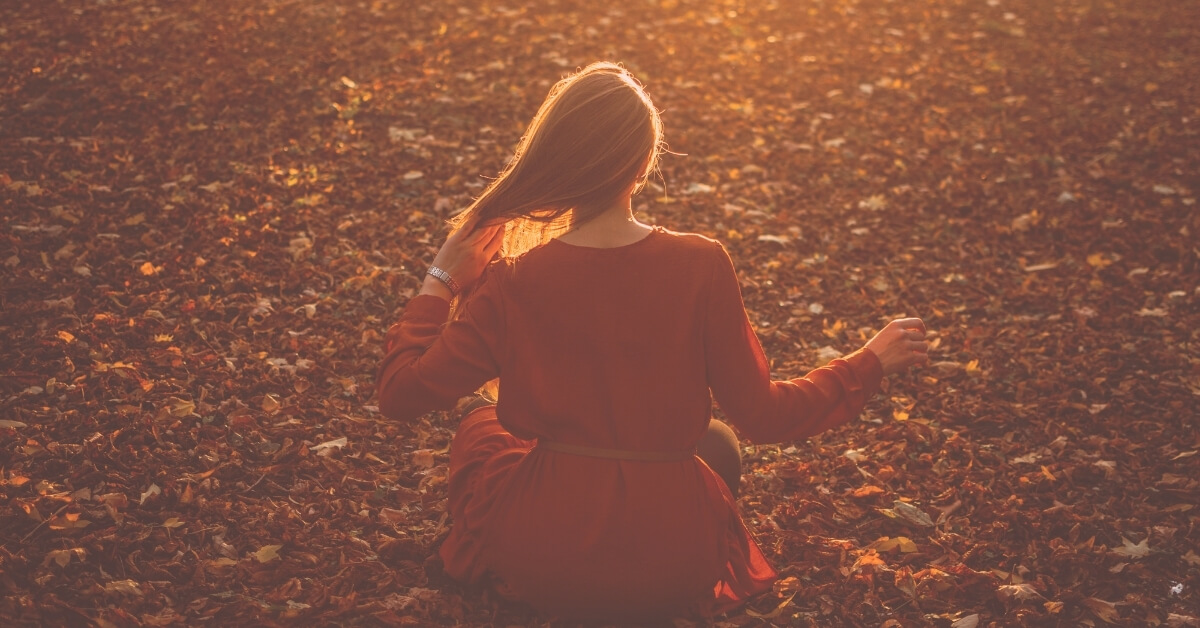 woman in red dress enjoys a quiet meditation among fall leaves