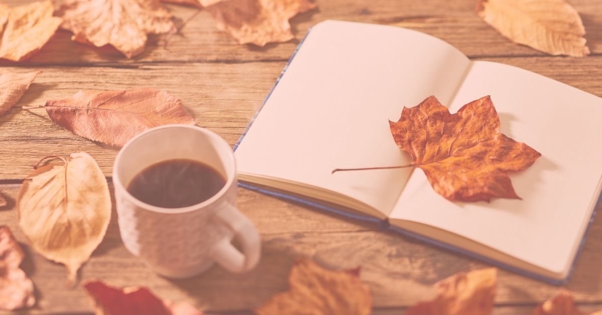 open journal and steaming coffee cup on table with colorful fall leaves